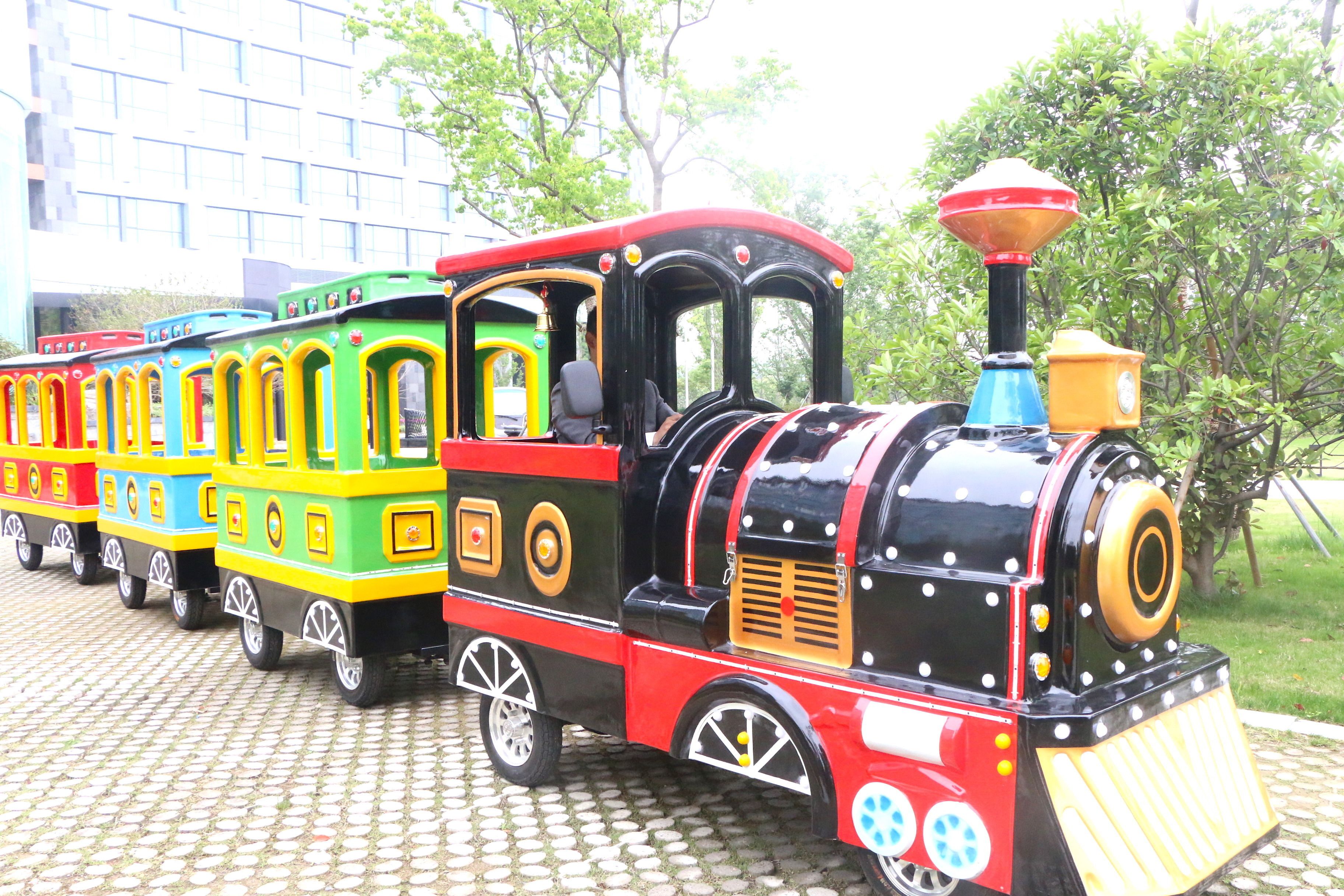 A colorful miniature train with a black engine and yellow, green, and red cars parked on a cobblestone path.