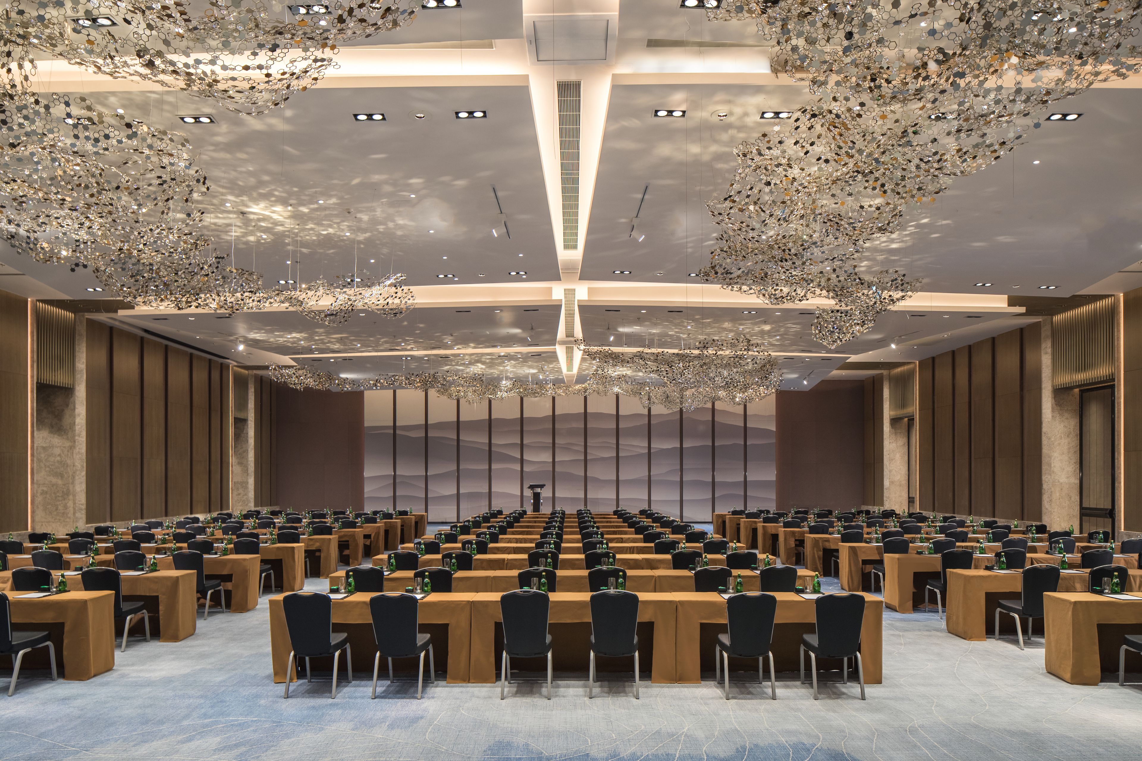 A conference room with multiple tables and chairs, a high ceiling with a decorative light fixture, and a large window in the background.