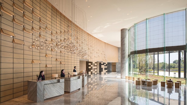 Un hall d’hôtel moderne doté d’un comptoir d’accueil, d’un espace salon et de grandes fenêtres offrant une vue sur l’extérieur.