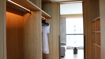 Een moderne hotelkamer met een houten garderobe, een zithoek met een tafel en stoelen, en een groot raam met uitzicht op de stad.