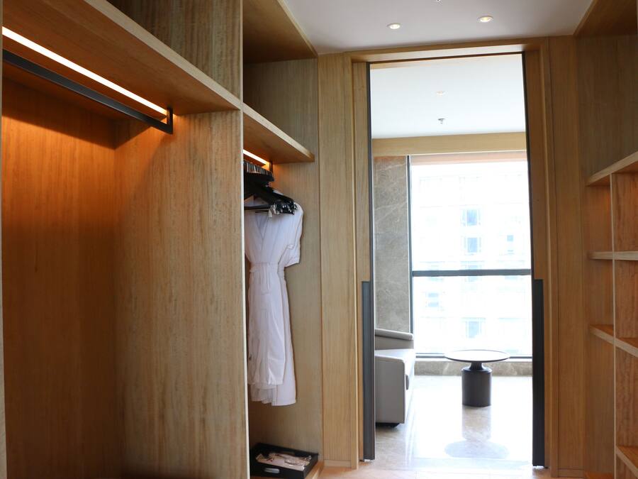 Een moderne hotelkamer met een houten garderobe, een zithoek met een tafel en stoelen, en een groot raam met uitzicht op de stad.