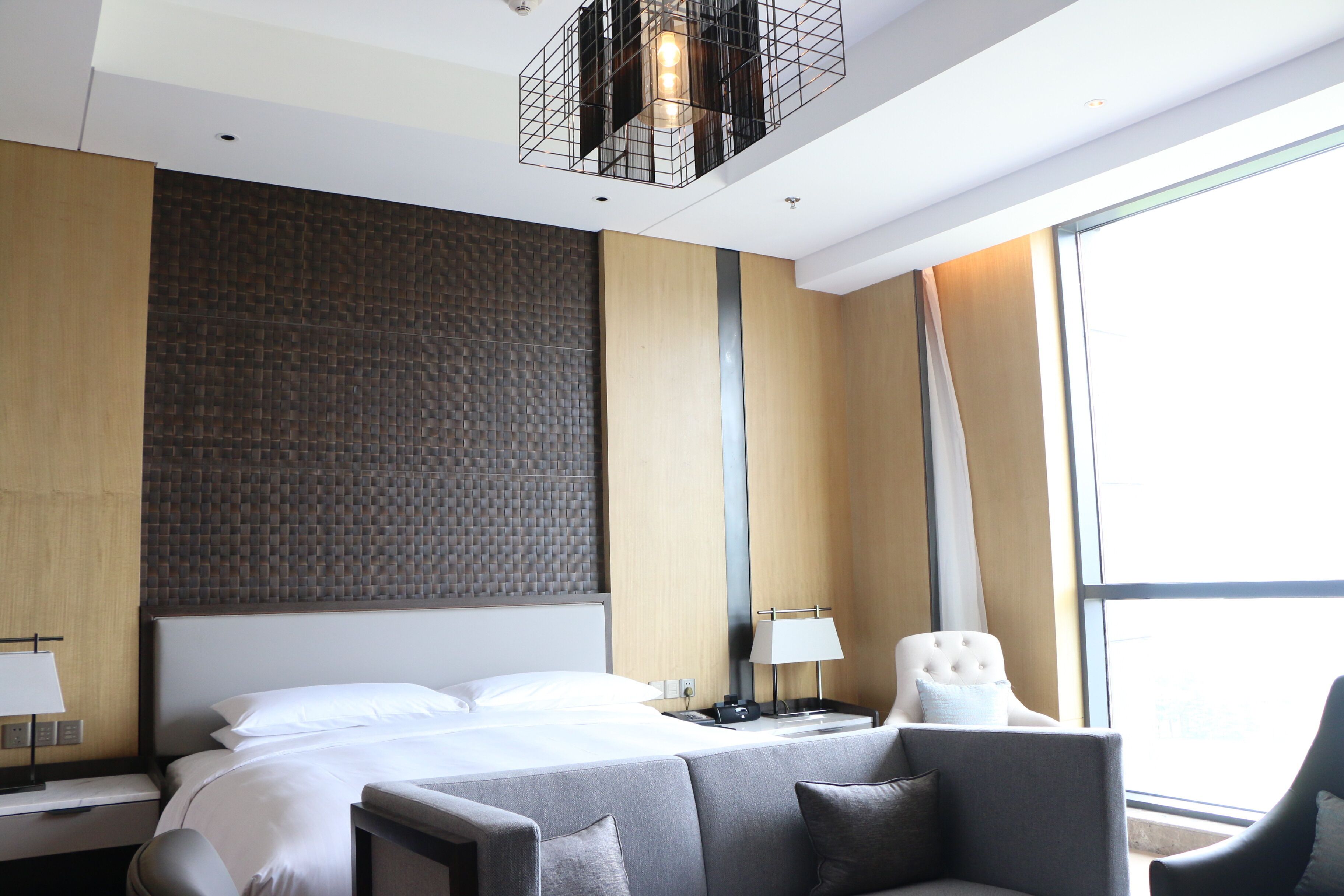 A modern hotel room with a large bed, a desk, a chair, and a large window.
