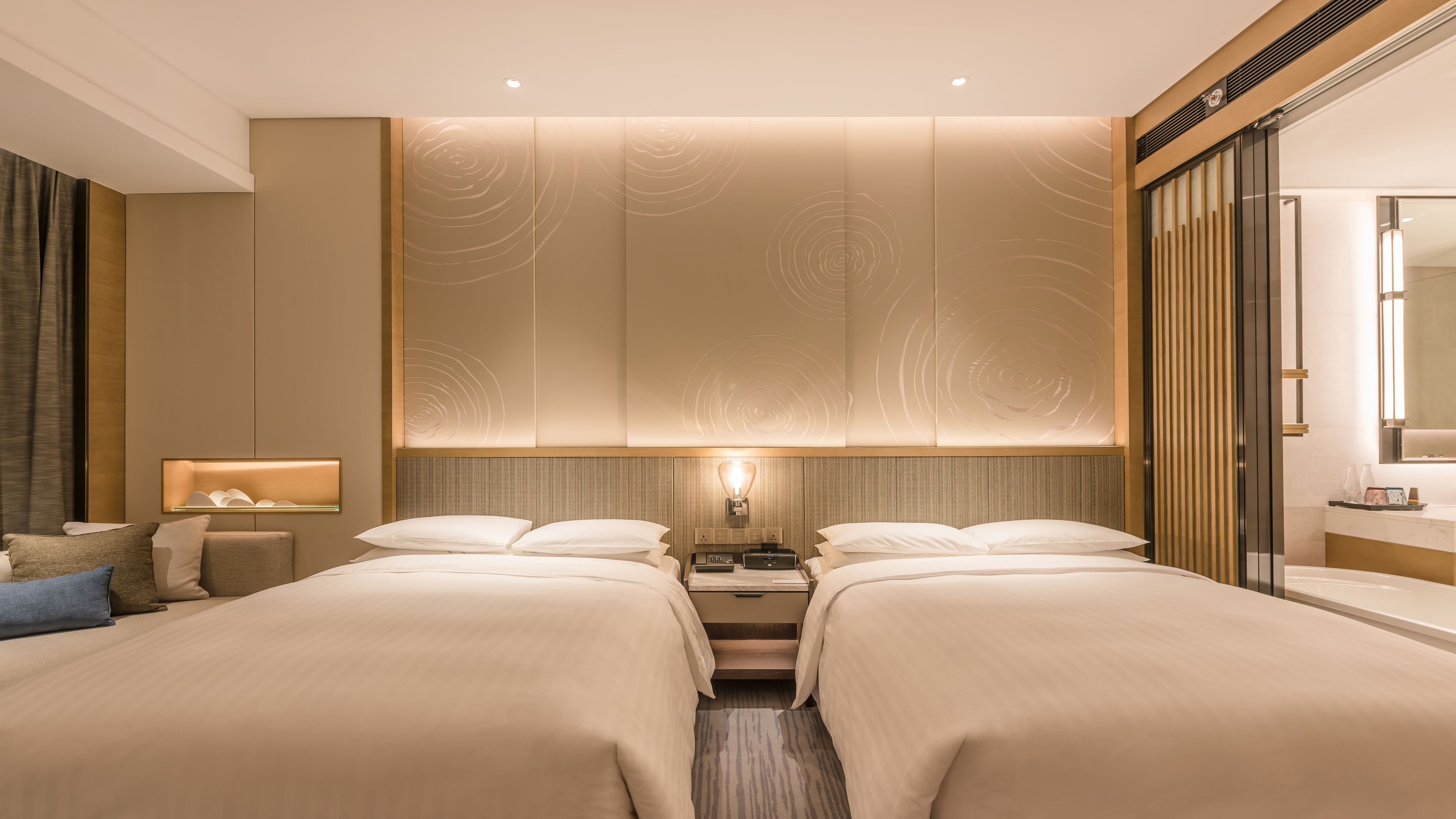 A hotel room with two beds, a nightstand, a lamp, and a large mirror.