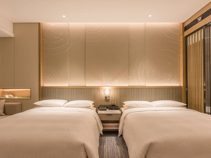 A hotel room with two beds, a nightstand, a lamp, and a large mirror.