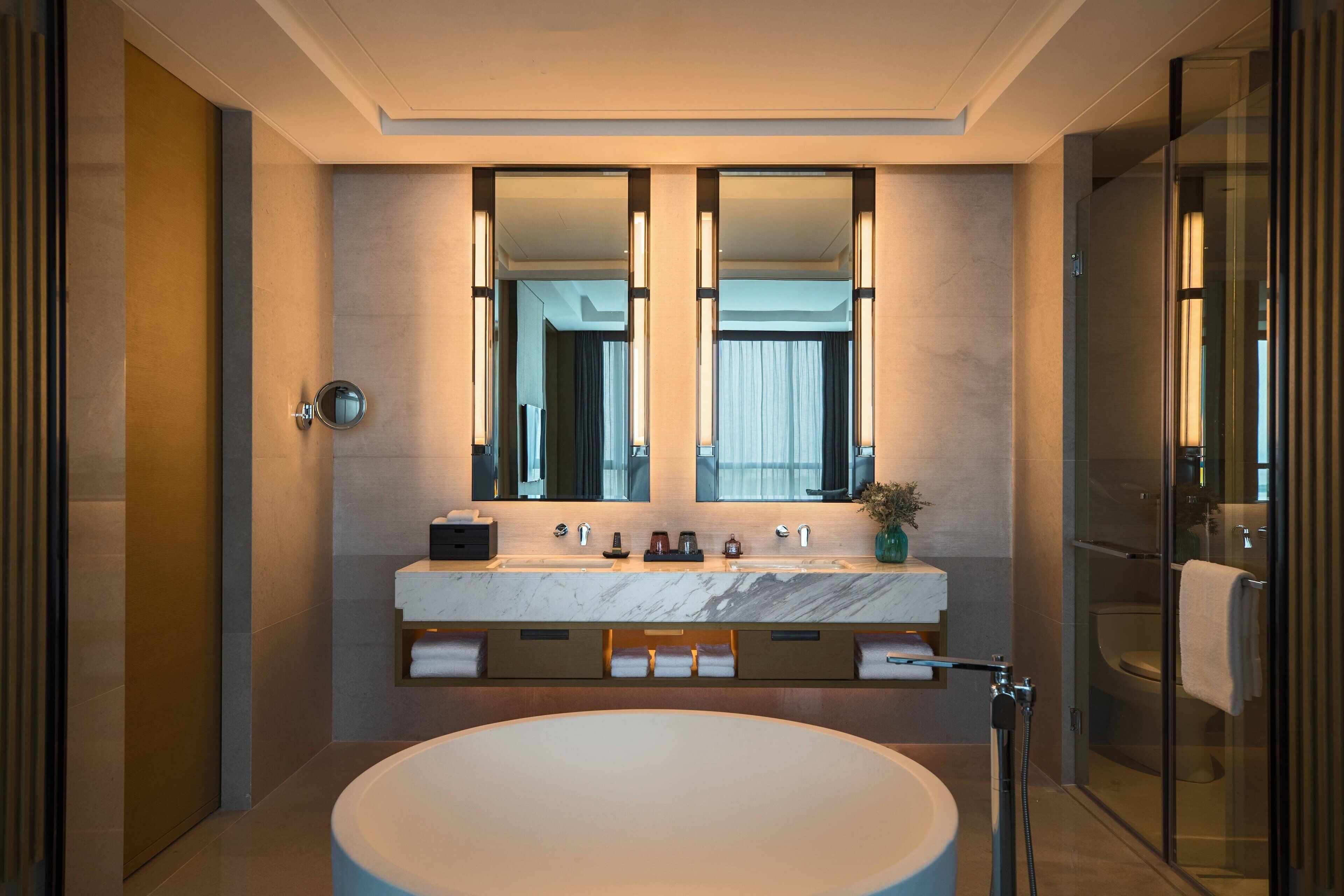 A modern bathroom with a large oval sink, dual mirrors, and a glass shower enclosure.