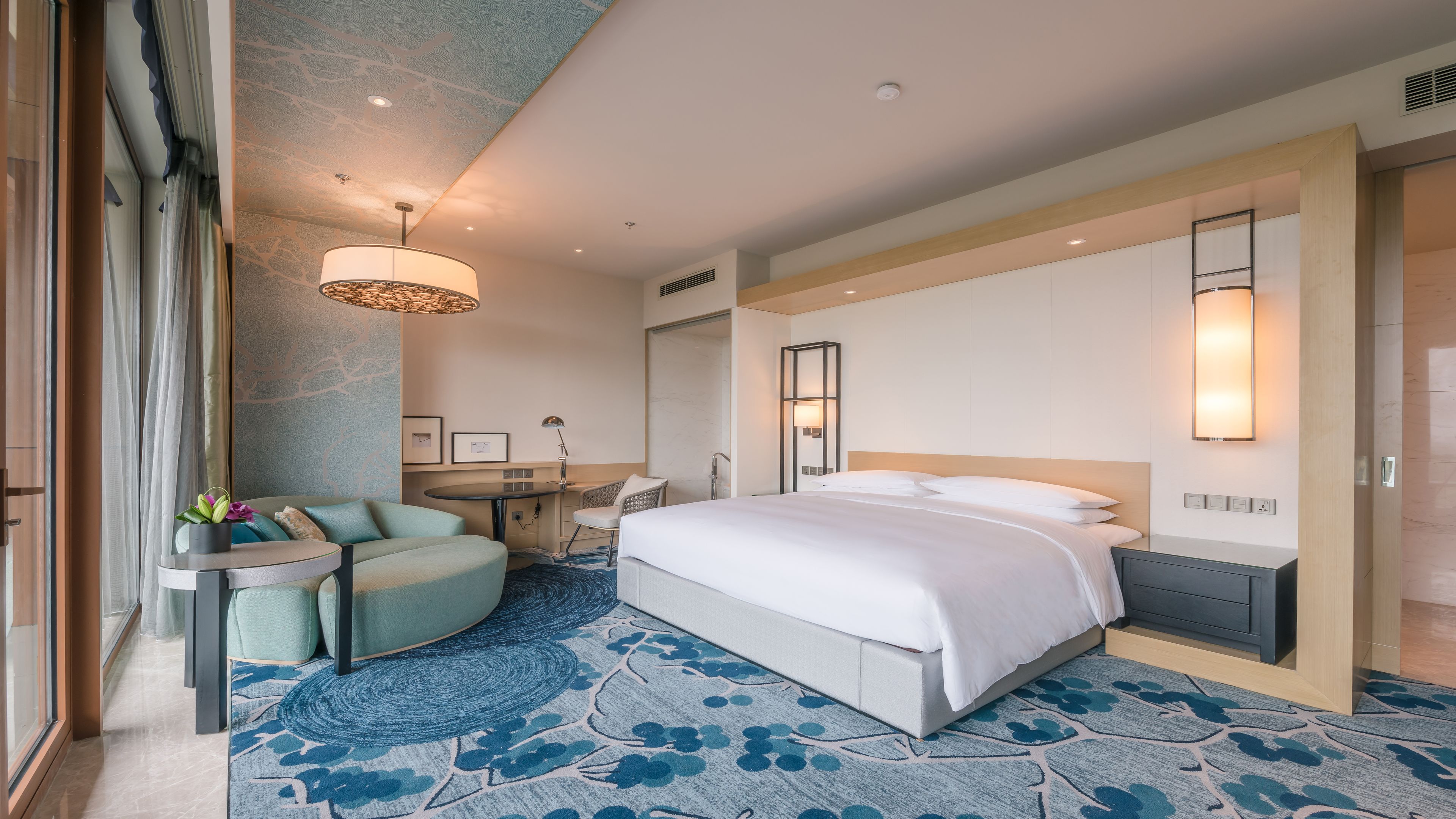 A modern hotel room with a large bed, a desk, and a seating area with a chair and a small table.