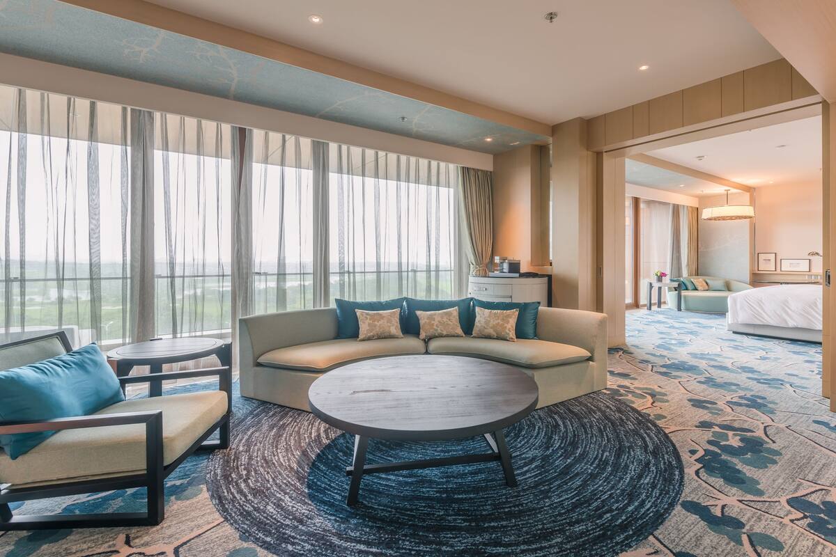 A modern hotel room with a sofa, armchair, and round table.