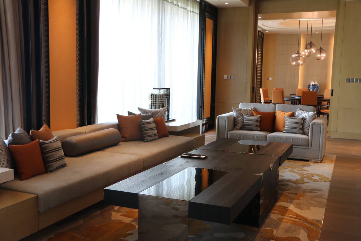 A modern living room with a large sofa, a coffee table, and a dining area with chairs and a table.