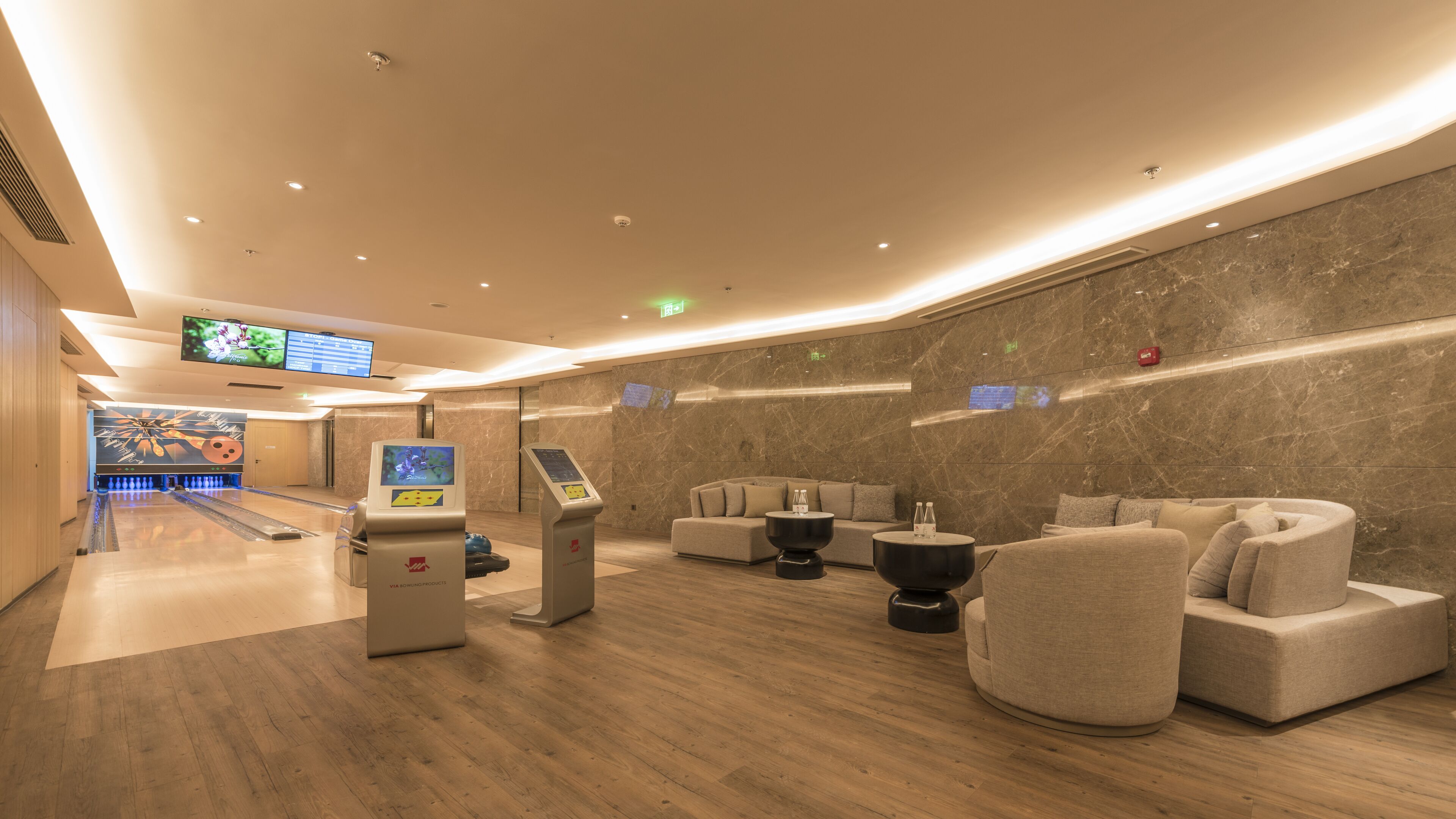 En moderne lobby med bowlingbane, siddeområde og digital skærm.