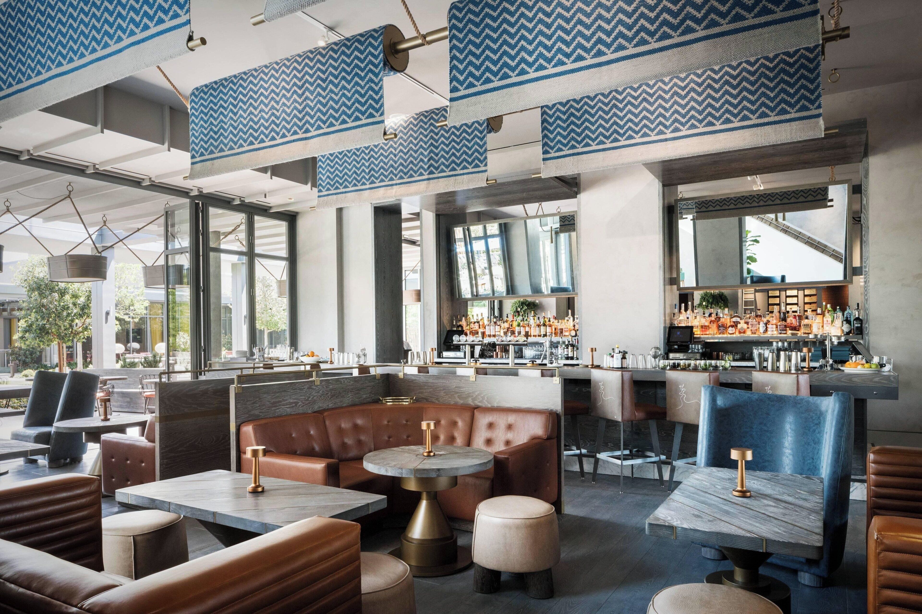 A modern restaurant interior with leather booths, round tables, and a bar area.