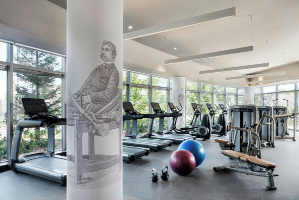 Un gimnasio con cintas de correr, elípticas y pesas libres.