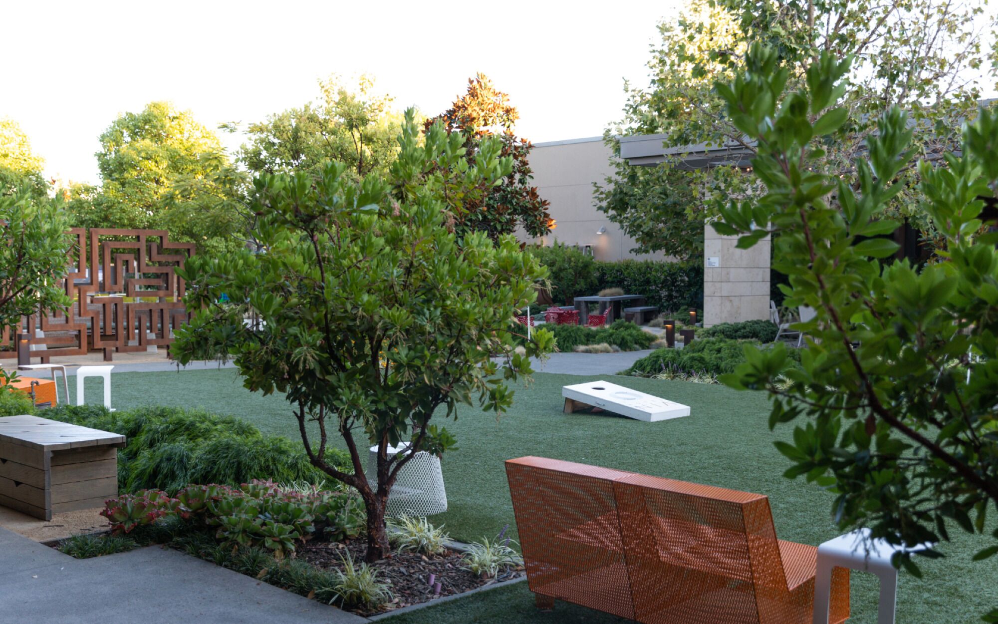 A landscaped garden with a wooden bench, a white table, and a geometric metal fence.