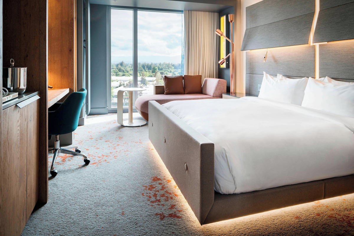 A modern hotel room with a large bed, a desk, and a view of the outdoors.
