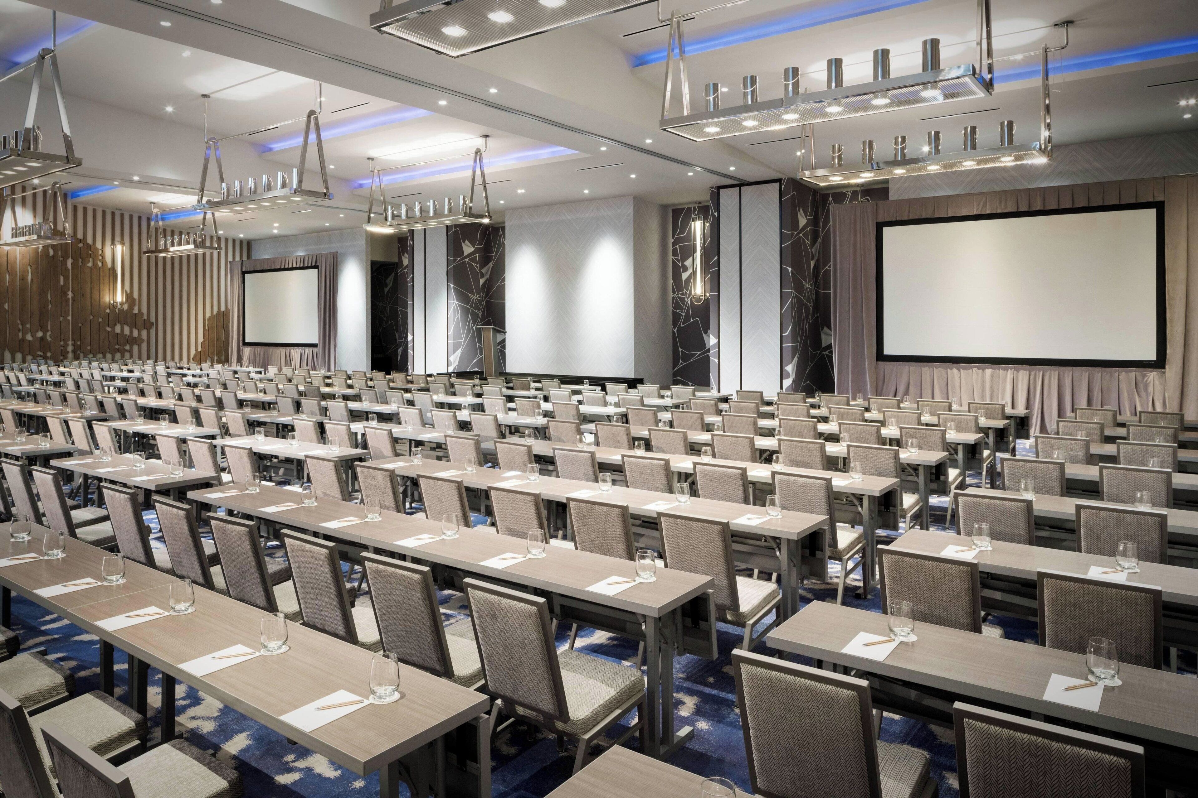 A conference room with rows of tables and chairs, a large screen, and modern lighting fixtures.