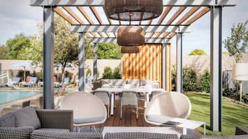 An outdoor patio with a pool, wicker furniture, and a pergola with hanging lamps.