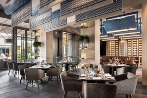 Un restaurante moderno con techos altos, cortinas azules y blancas estampadas y diferentes opciones de asientos.