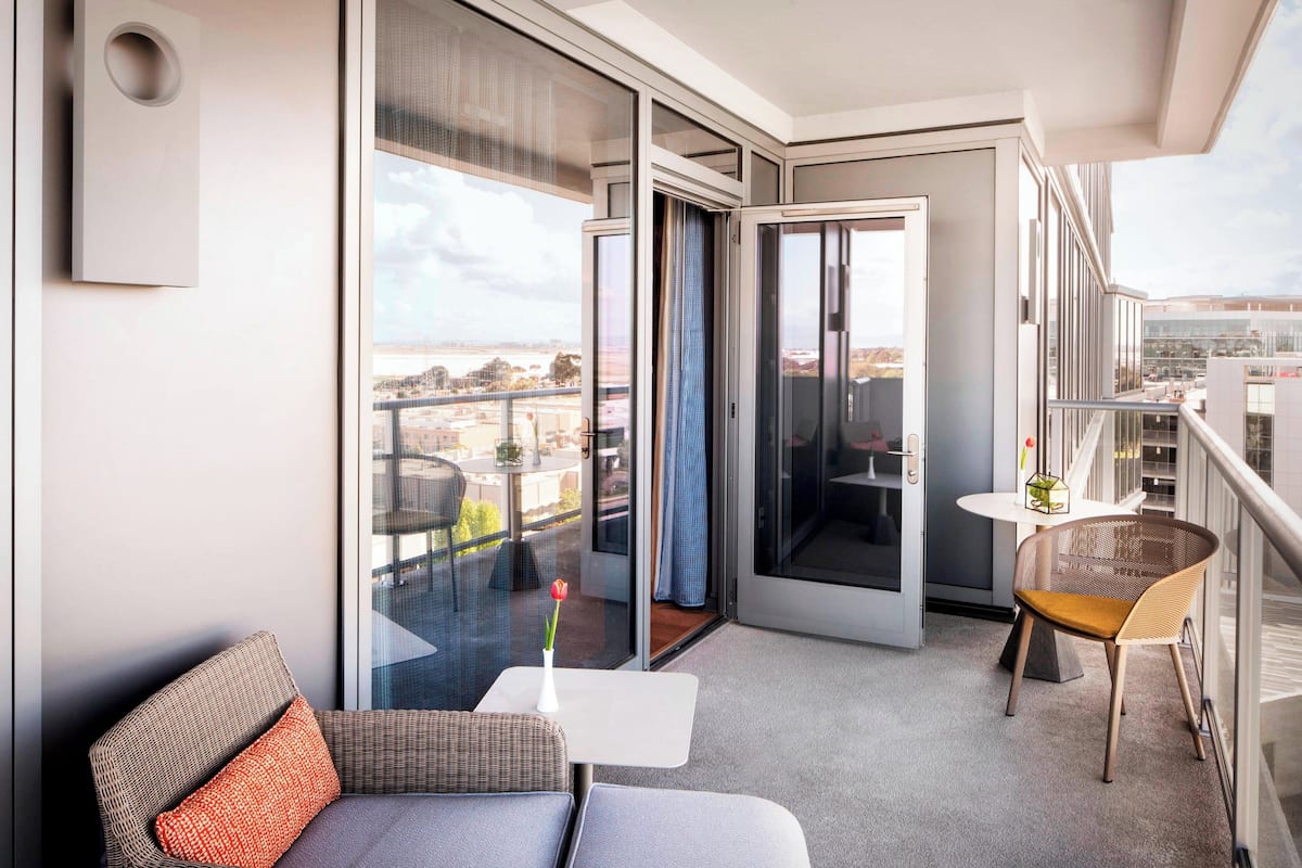 A modern balcony with a sofa, a small table, and a chair, offering a view of the cityscape.