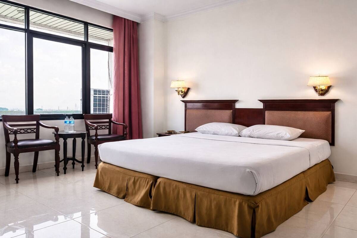 Ein Hotelzimmer mit einem Bett, zwei Sesseln, einem kleinen Tisch und zwei Wandlampen.