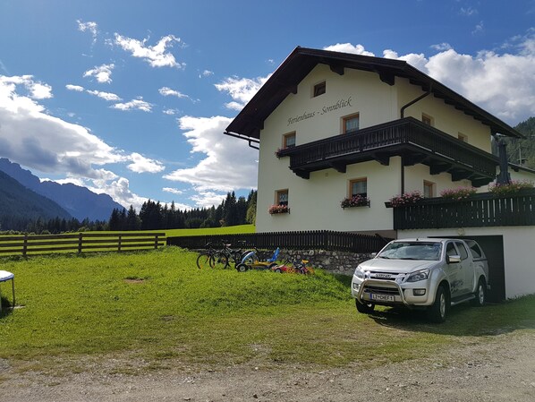 A two-story building with a balcony, a parked car, and a mountain backdrop. - Ferienhaus-Sonnblick (Sillian)