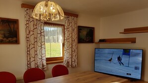 Comedor con mesa de madera, sillas rojas, una araña y un televisor mostrando una escena de esquí.