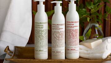 Three bottles of Malin+Goetz shampoo on a tray with a bar of soap and a towel.
