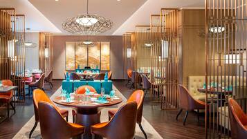 Un espace repas moderne avec des tables rondes, des chaises orange et une table bleue au centre.
