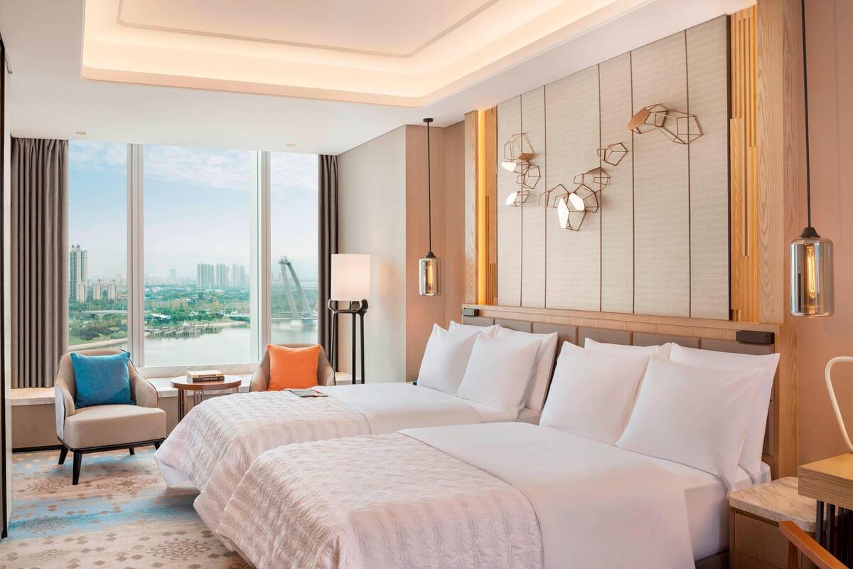 Ein Hotelzimmer mit zwei Betten, Stadtblick, einem modernen Kronleuchter und einem großen Fenster mit Vorhängen.