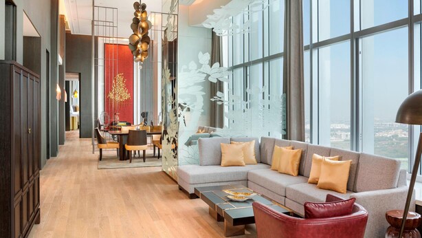 A modern living room with a grey sofa, red armchair, and wooden coffee table. A dining area with a table and chairs is visible in the background. - Le Meridien Xi'an Chanba (Xi'an)