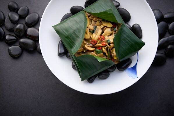 A white plate with a dish wrapped in green leaves, surrounded by black stones. - Le Meridien Xi'an Chanba (Xi'an)