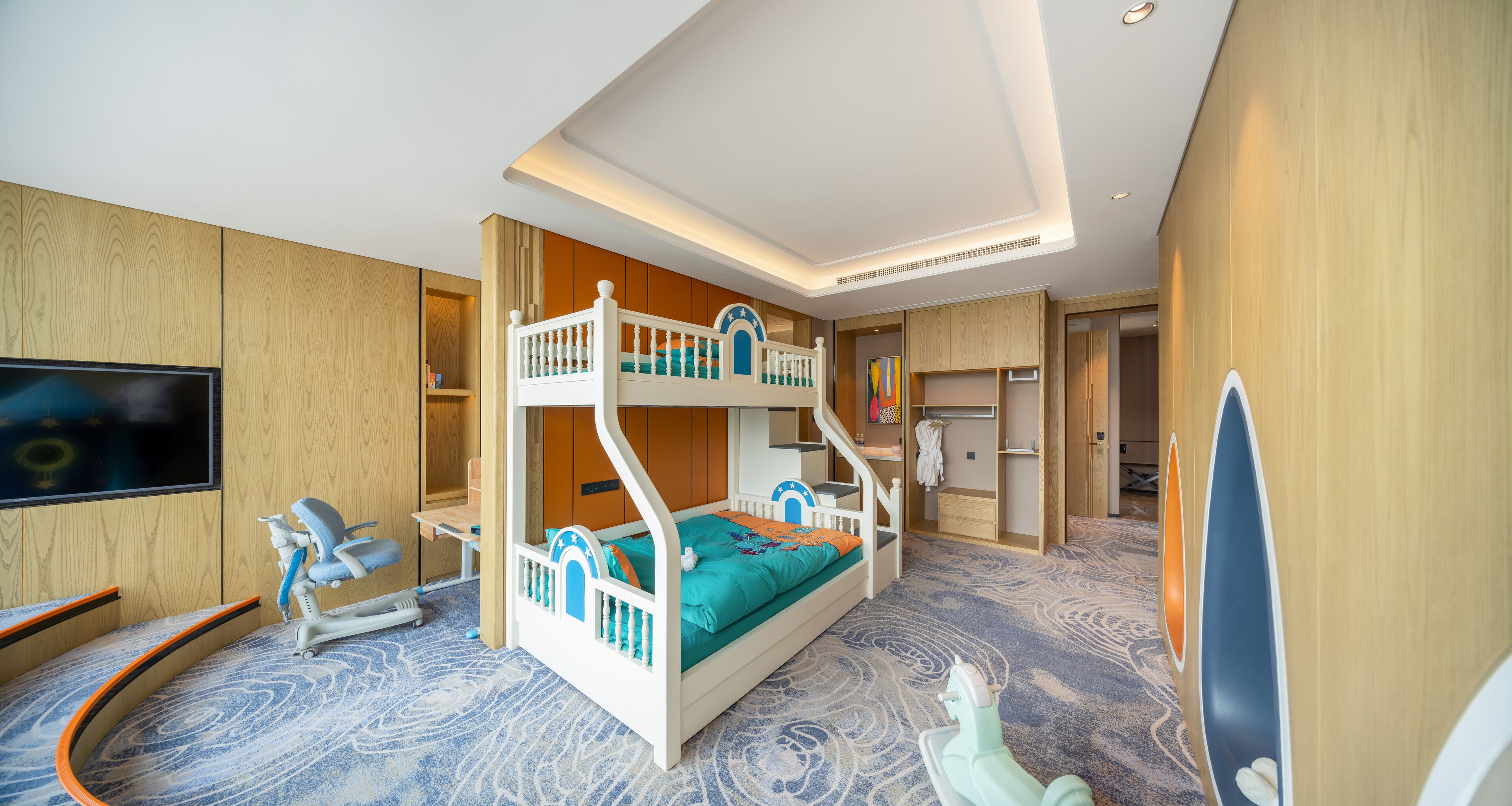 Een stapelbed met een televisie, een bureau en een stoel in een kamer met houten wanden en een kamerbreed tapijt met dessin.