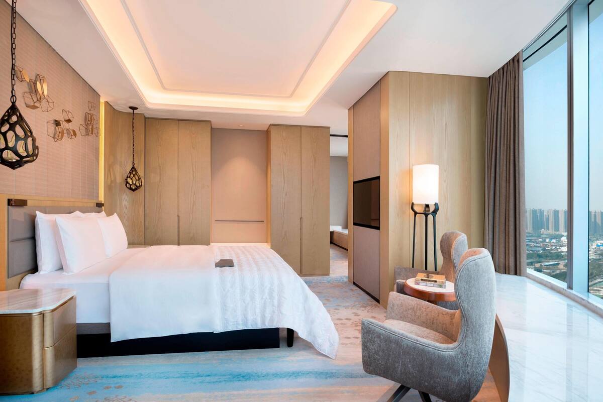 Ein modernes Hotelzimmer mit einem großen Bett, einer Sitzecke und Blick auf die Stadt.