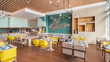 Interior de un restaurante moderno con sillas amarillas, techo de madera y una obra de arte mural de mosaico.
