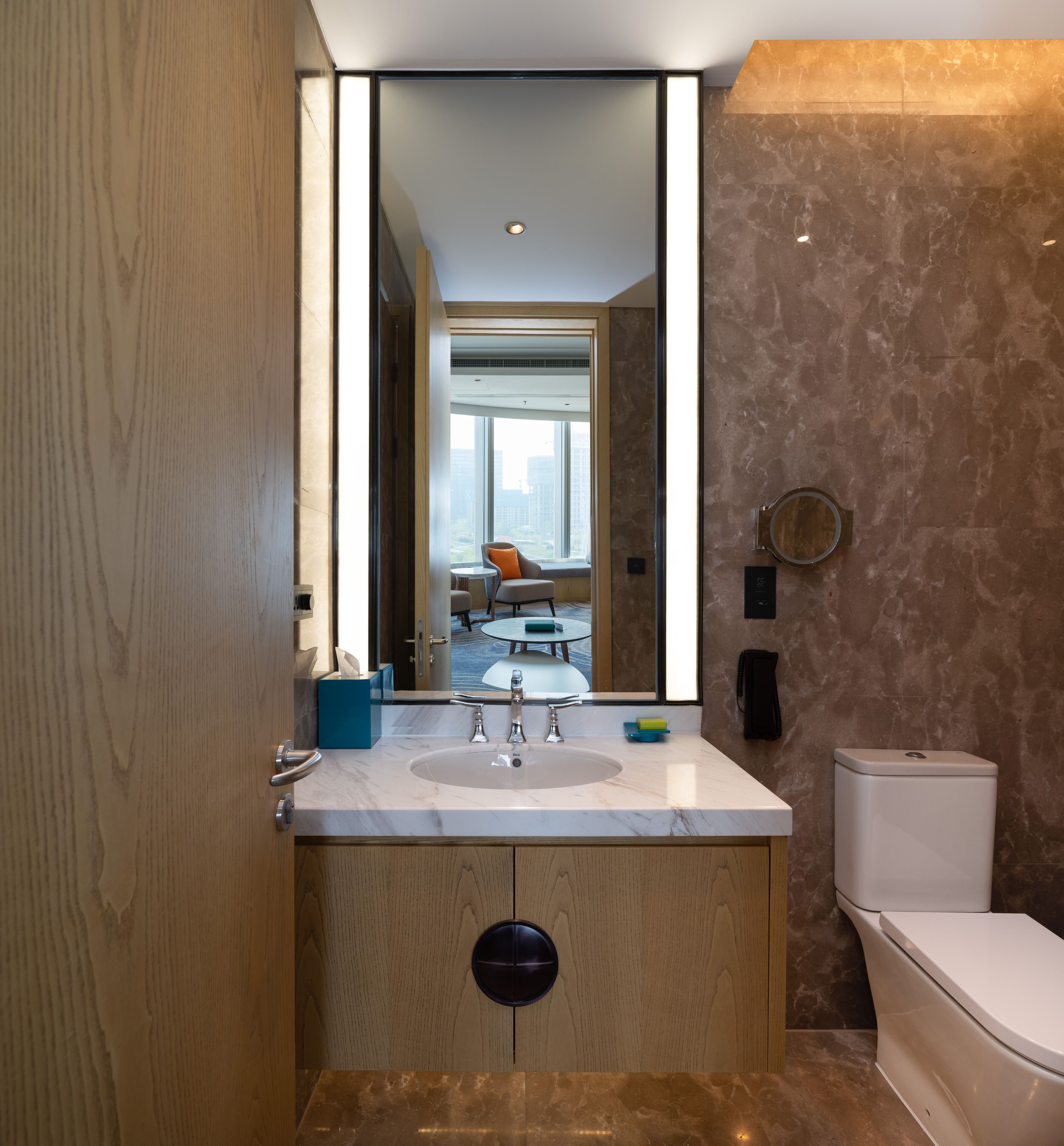 A modern bathroom with a marble sink, a toilet, and a large mirror.