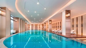 A large indoor swimming pool with a tiled floor, surrounded by lounge chairs and a modern ceiling design. - Le Meridien Xi'an Chanba (Xi'an)
