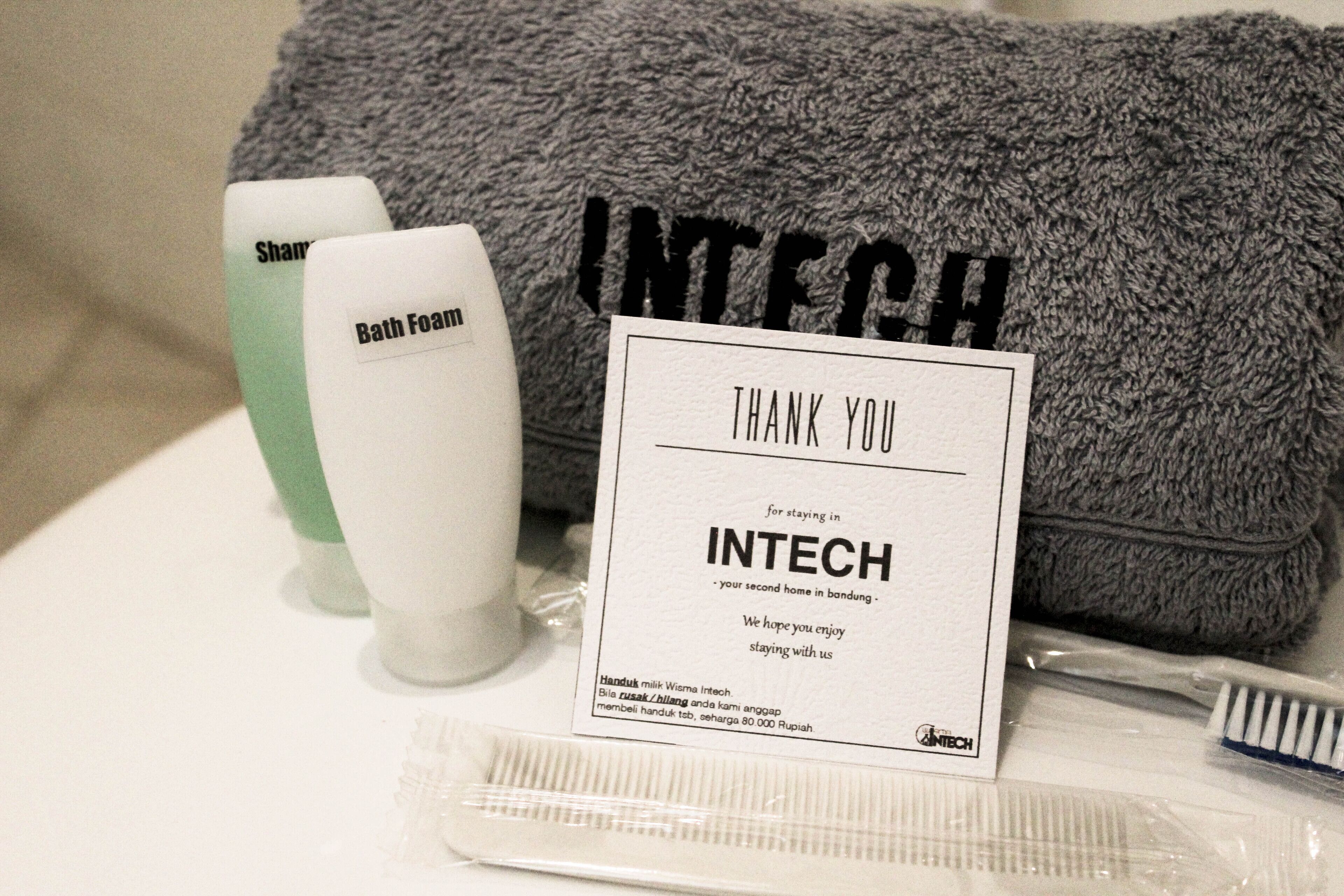 Toiletries including a bath foam bottle, a toothbrush, and a comb, along with a towel and a thank you card from INTECH.