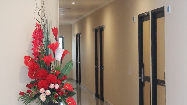 A hallway with a floral arrangement on a stand, doors, and a polished floor. - Intech Hostel (Bandung)
