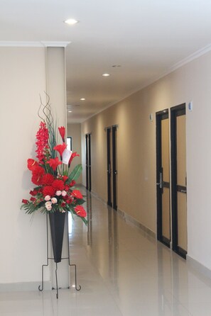 A hallway with a floral arrangement on a stand, doors, and a polished floor. - Intech Hostel (Bandung)