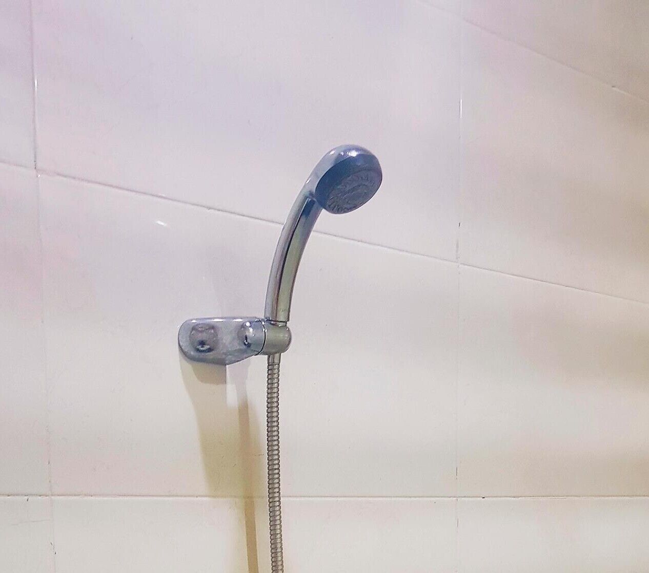 A showerhead with a flexible hose, mounted on a tiled wall.