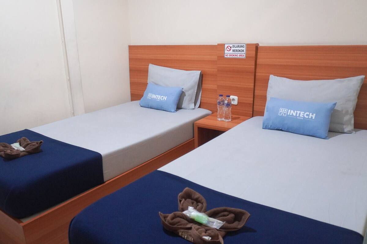 A hotel room with two single beds, each with a blue pillow and a sign indicating a no smoking area.