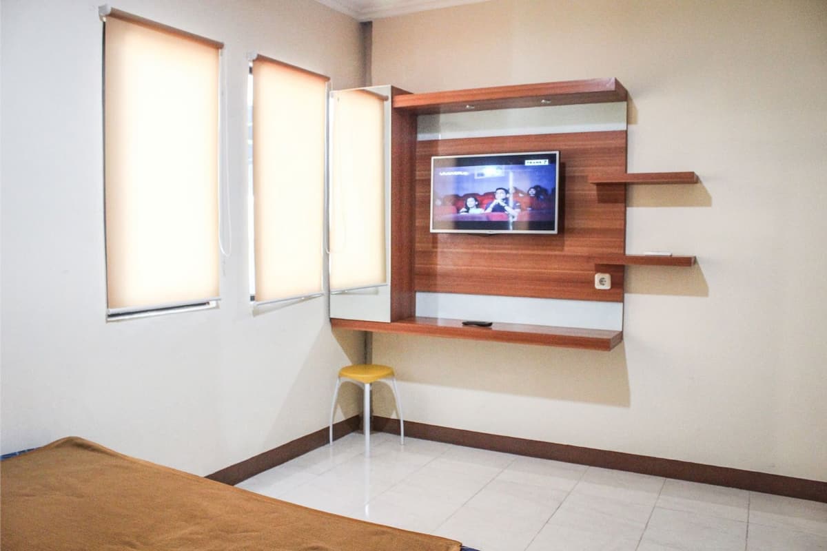 A room with a TV mounted on a wooden wall, a small stool, and a bed.