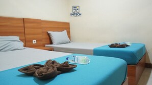 A hotel room with two beds, each with a blue bedspread and pillows. There is a water bottle and slippers on the beds. - Intech Hostel (Bandung)