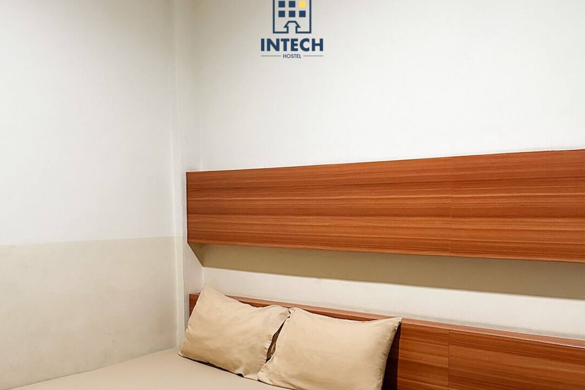 A single-bed room with a wooden headboard, a small bedside table, and a wall-mounted logo.