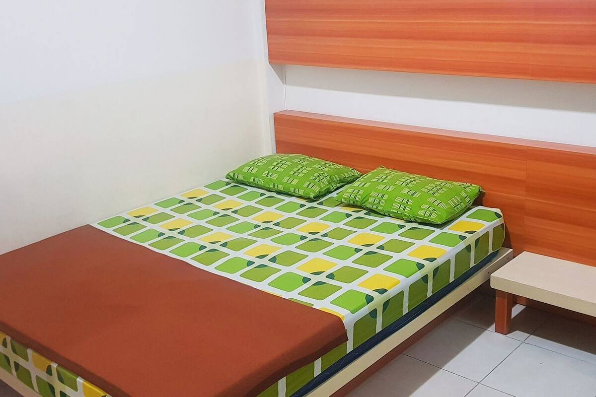 A small, single-bed room with a wooden headboard, a patterned bedspread, and a bench.