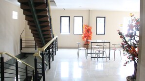 A spacious living area with a staircase, a dining table with chairs, and a potted plant. - Intech Hostel (Bandung)