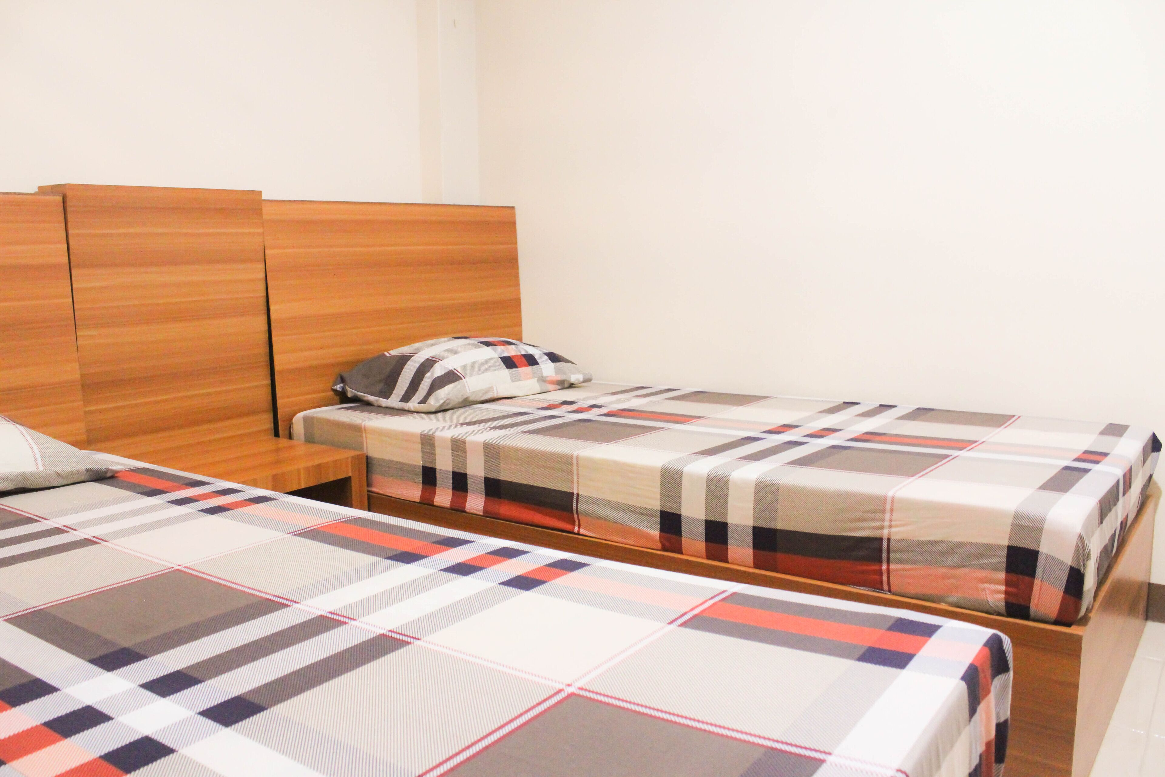 Camera d'albergo con due letti, ciascuno con copripiumino a quadri, una testiera in legno e un comodino con una lampada.