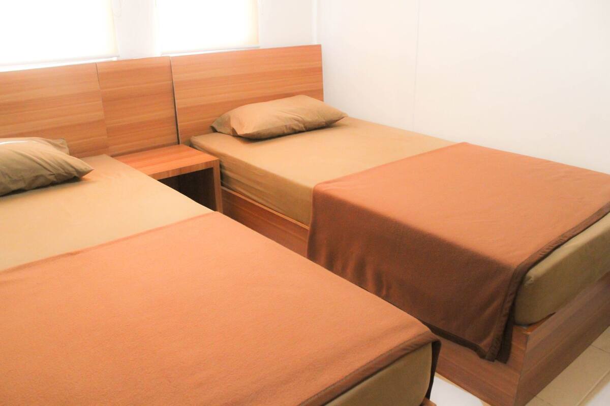 A room with three single beds, each with a wooden headboard and a brown bedspread.