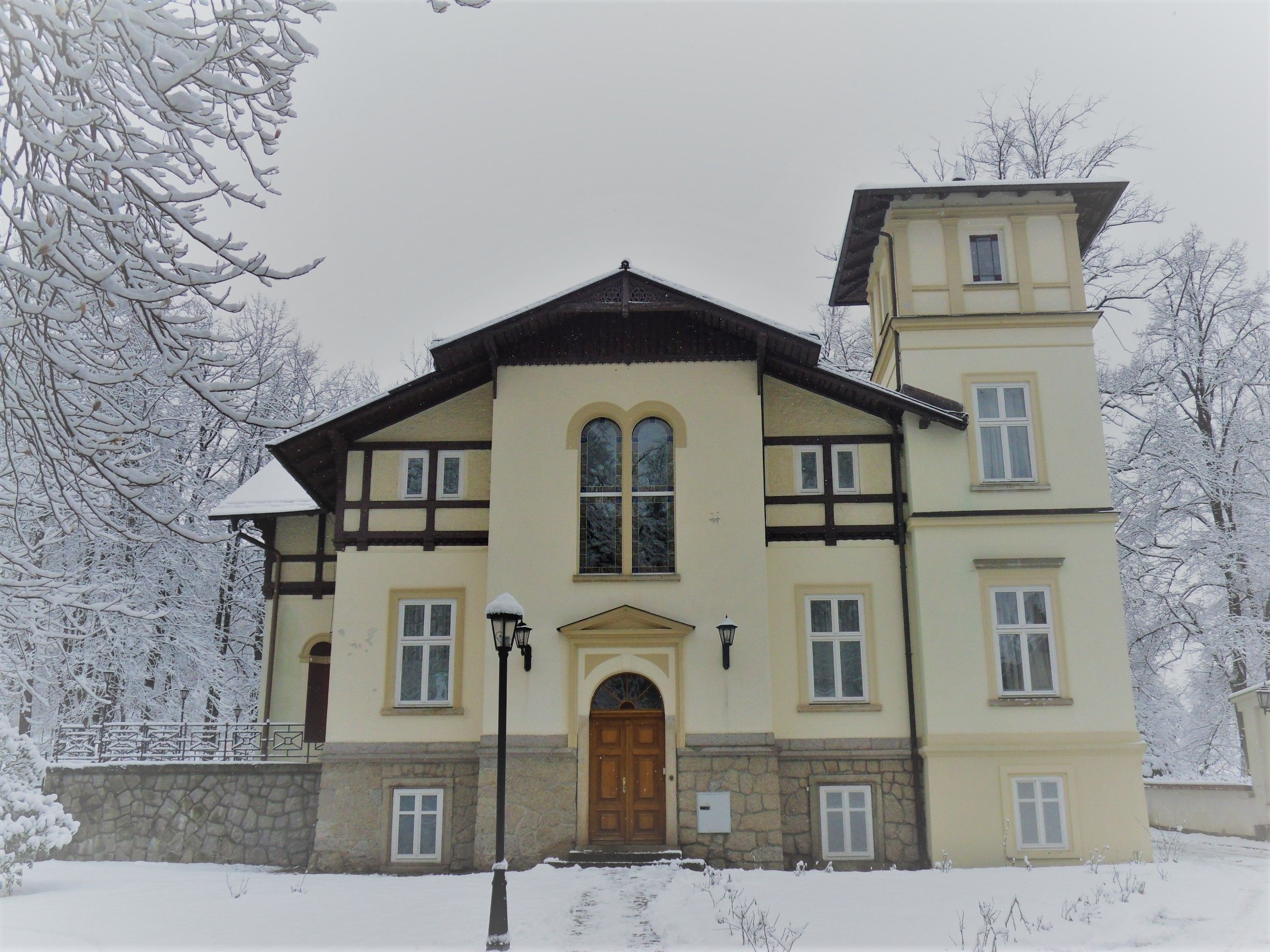 Un grand bâtiment à deux étages, doté d’une façade symétrique, avec une entrée centrale ornée d’une porte en bois et d’un socle en pierre.