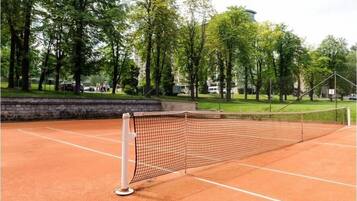 A tennis court with a net, surrounded by trees and a stone wall.