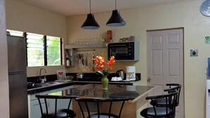 A kitchen with a central island, black bar stools, a microwave, and a refrigerator.