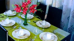 A dining table set with plates, glasses, and a vase of red flowers.